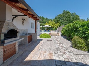 Un espace patio agrémenté d’une cheminée en pierre, de sièges d’extérieur et d’une piscine en arrière-plan.
