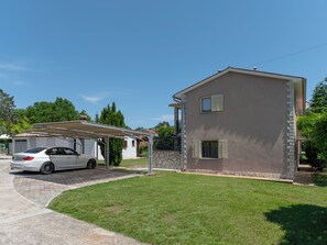 Un bâtiment à deux étages doté d’un abri pour voiture, d’une façade en pierre et surplombant un ciel dégagé.