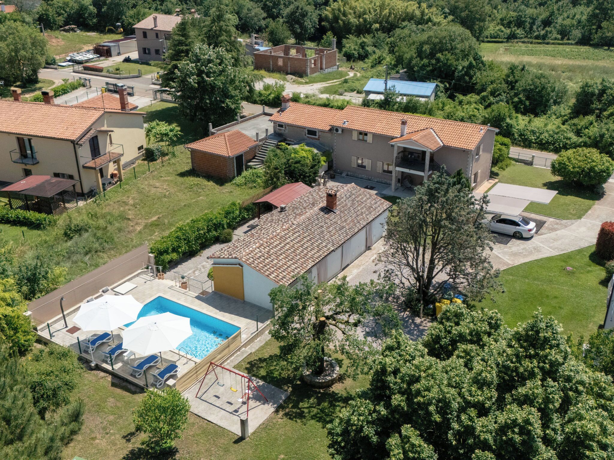 Un barrio residencial con piscina, columpio y un coche aparcado en la entrada.