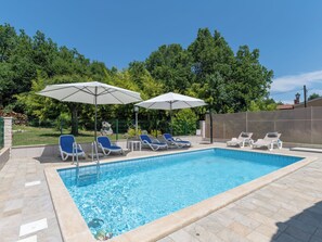 Une piscine entourée d’une clôture et d’arbres, avec des chaises longues et des parasols.