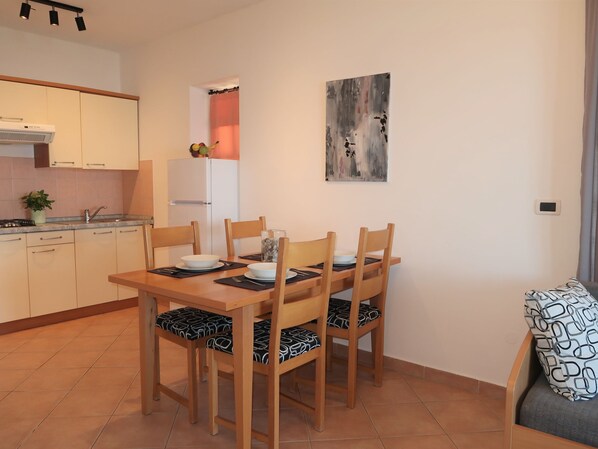 A compact kitchen with a dining area, including a table set for four with chairs, a refrigerator, a sink, and a stove. - Apartment Ulika by Interhome (Labin)
