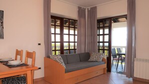 A cozy room with a sofa, dining table, chairs, and large windows with curtains.