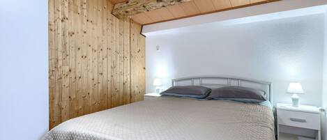 A bedroom with a wooden ceiling, a bed with a quilted cover, two bedside lamps, and a nightstand.