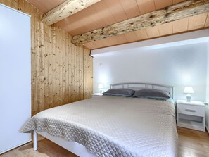 Une chambre à coucher avec un plafond en bois, un lit recouvert d’une courtepointe, deux lampes de chevet et une table de chevet.