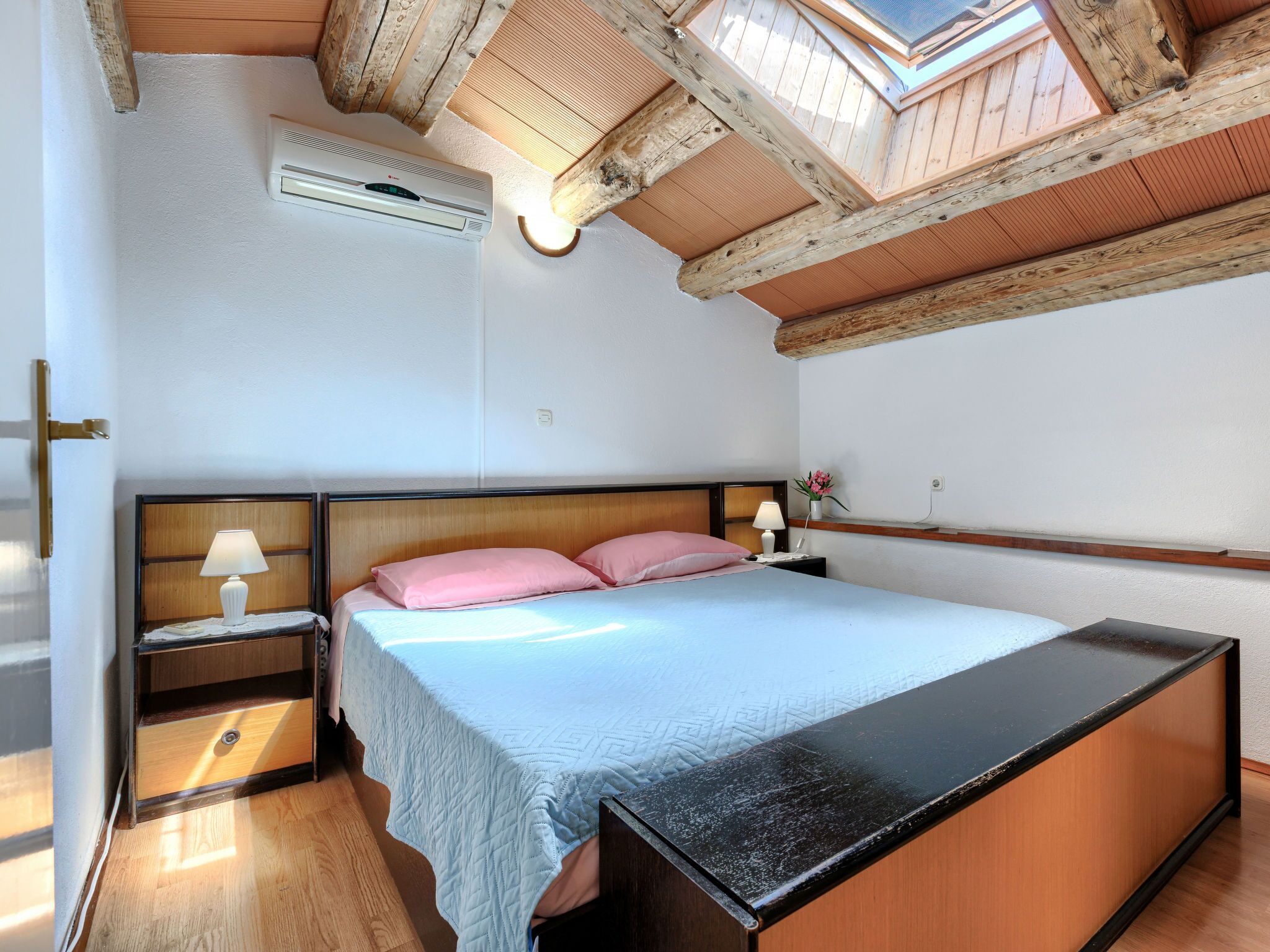 A bedroom with a bed, bedside tables, a lamp, and a skylight.