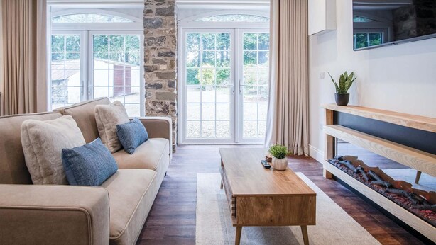 A modern living room with a beige sofa, a wooden coffee table, and a TV mounted on the wall. - The Carthouse - 1 Bedroom Cottage - Princes Gate (Narberth)