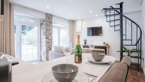 A modern dining area with a wooden table, two bowls, a bottle of champagne, and a sofa. - The Carthouse - 1 Bedroom Cottage - Princes Gate (Narberth)