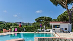 A swimming pool with stone mosaic borders, lounge chairs, and umbrellas.