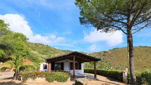 A small, single-story building with a porch, surrounded by a gravel driveway and lush greenery. - Panorama by Interhome (Capoliveri)