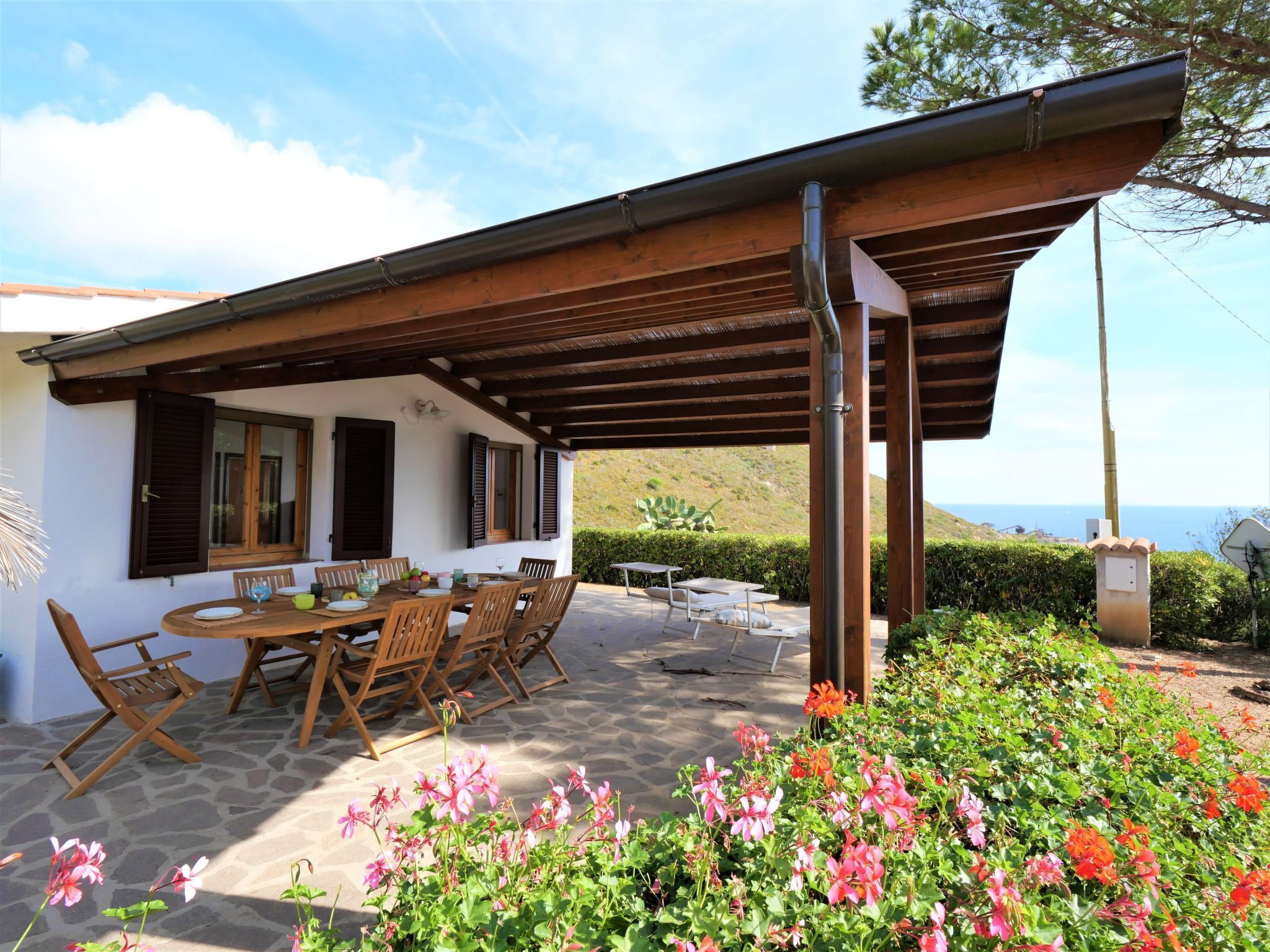 Un patio cubierto con una mesa y sillas, piso de piedra y plantas con flores.