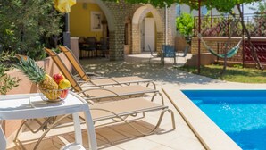 Un área junto a la piscina con sillones de descanso, una mesa con frutas y una hamaca.