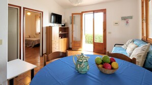 A room with a dining table, chairs, a television, and a window with a view of greenery. - Panorama I by Interhome (Capoliveri)