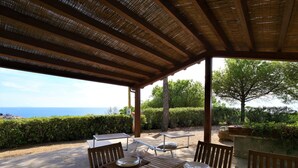 An outdoor dining area with a view of the sea, covered by a wooden pergola, and furnished with tables and chairs. - Panorama I by Interhome (Capoliveri)