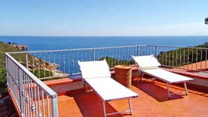 Une terrasse avec deux chaises longues blanches et un panier en osier, offrant une vue sur la côte.