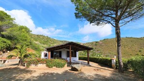 Une petite maison dotée d’une pergola en bois, entourée d’une allée gravillonnée et d’une végétation luxuriante.