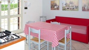 Ett kök med en gasspis, ett bord med en röd- och vitrutig duk och en röd soffa. Det finns tre tavlor på väggen.