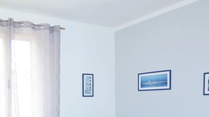 Ett hotellrum med två sängar, ett fönster med gardiner och två inramade tavlor på väggen.