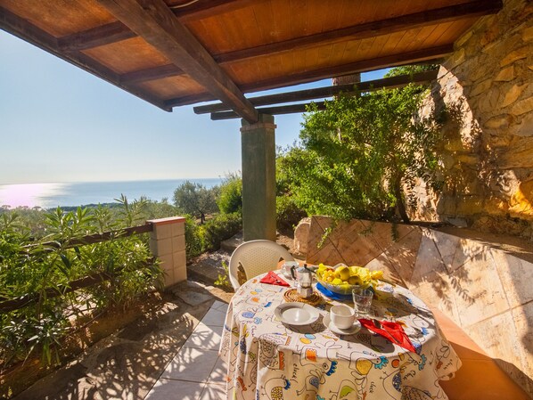 Un espace extérieur aménagé pour prendre les repas, avec une table dressée pour deux personnes, offrant une vue panoramique sur la mer.