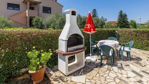 Eine Terrasse im Freien mit Steinplattenboden, einem Pizzaofen, einem Tisch mit Stühlen und einem roten Sonnenschirm.