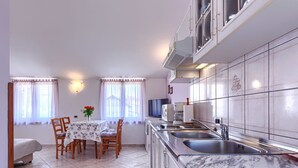 Eine kompakte Küche mit Marmorarbeitsplatte, ein Essbereich mit Tisch und Stühlen sowie ein Fernseher an der Wand.