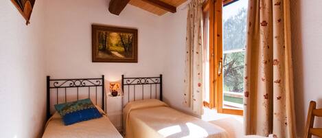 A bedroom with two single beds, a wooden ceiling, a painting on the wall, and a window with curtains.