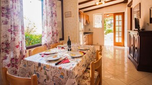 A dining area with a table set for four, a kitchen in the background, and a view of greenery outside. - Piccola Oasi 4 by Interhome (Capoliveri)