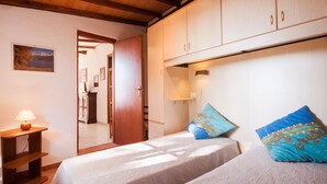 A bedroom with two beds, a nightstand, a lamp, and a wardrobe. - Piccola Oasi 4 by Interhome (Capoliveri)