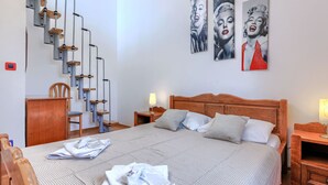 A bedroom with a bed, wooden headboard, two bedside tables, a chair, a desk, a staircase, and three wall art pieces. - VIlla Eldina by Interhome (Pula)