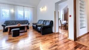 A modern living room with a wooden floor, black leather sofas, a wooden coffee table, and a dining area with a table and chairs. - VIlla Eldina by Interhome (Pula)