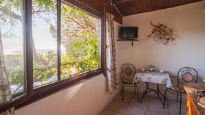 A cozy room with a large window, a television mounted on the wall, a small table with chairs, and a view of greenery outside. - Piccola Oasi 6 by Interhome (Capoliveri)