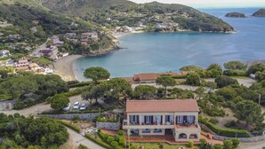 Eine Küstenvilla mit Terrakotta-Dach, umgeben von üppigem Grün und einem Strand.