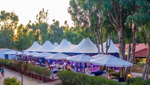 An outdoor dining area with multiple white tents and tables, surrounded by greenery and trees. - Camping Village Laguna Blu by Interhome (Alghero)