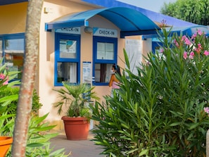 A check-in area with blue signage, a palm plant, and a person wearing a mask.