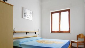 A bedroom with a bed, a chair, a window, and a painting on the wall. - Reale Marina (REI207) by Interhome (Costa Rei)