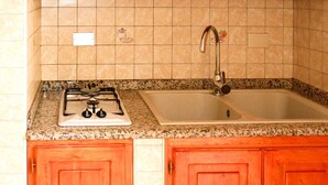 A kitchen with a gas stove, a sink, and wooden cabinets. - Rei Marina Fronte Mare (REI204) by Interhome (Costa Rei)