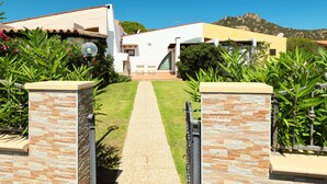 A modern house with a stone pathway leading to the entrance, surrounded by lush greenery and a mountain in the background. - Mirto Marino (REI410) by Interhome (Costa Rei)