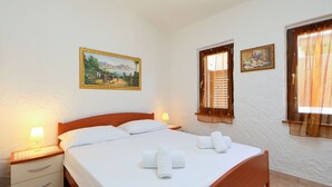 A neatly made bed with white linens and two rolled towels, a wooden nightstand with a lamp, and a wall with two framed paintings. - Mirto Marino (REI410) by Interhome (Costa Rei)