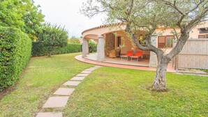A covered outdoor seating area with stone pillars, a stone pathway, and a well-maintained lawn. - Rei Sole (REI303) by Interhome (Costa Rei)