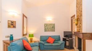 A living room with two blue sofas, a small table, a TV, and a fireplace. - Rei Sole (REI303) by Interhome (Costa Rei)