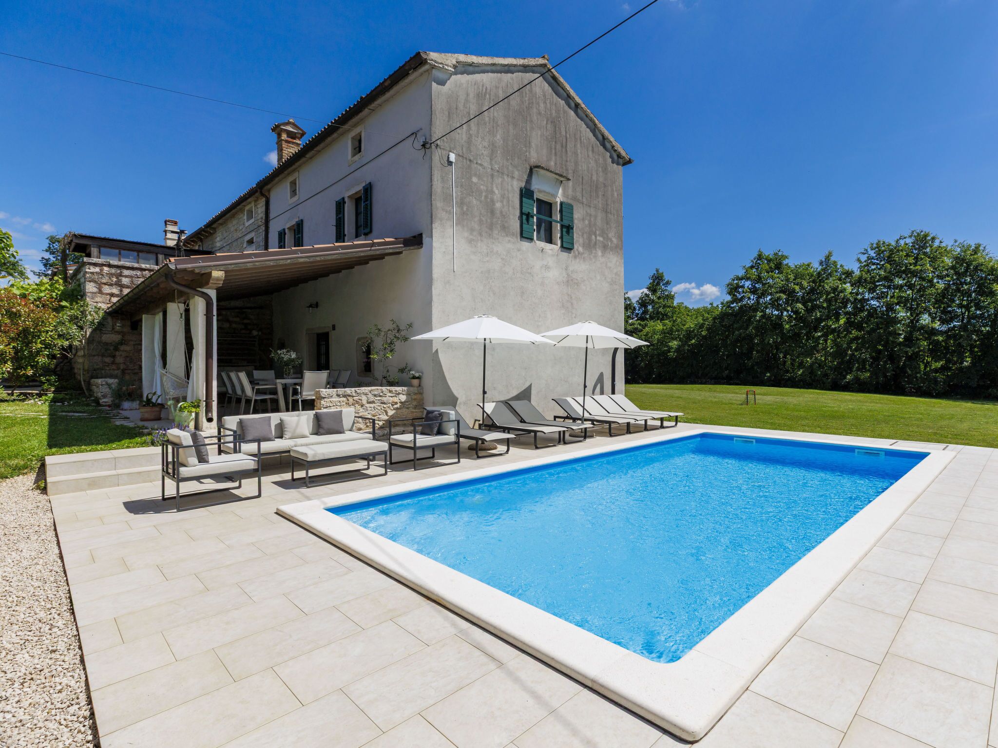A modern house with a swimming pool, outdoor seating, and a stone wall.
