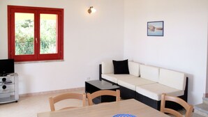 Quarto com uma mesa de jantar, cadeiras, um sofá, uma TV e uma janela com moldura vermelha.