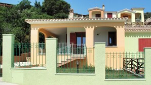 Uma casa de dois andares com varanda, escadaria e cerca verde.