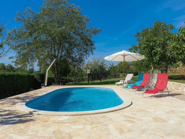 A swimming pool with stone tiles, surrounded by lounge chairs and an umbrella. - Jadranka by Interhome (Rovinj)