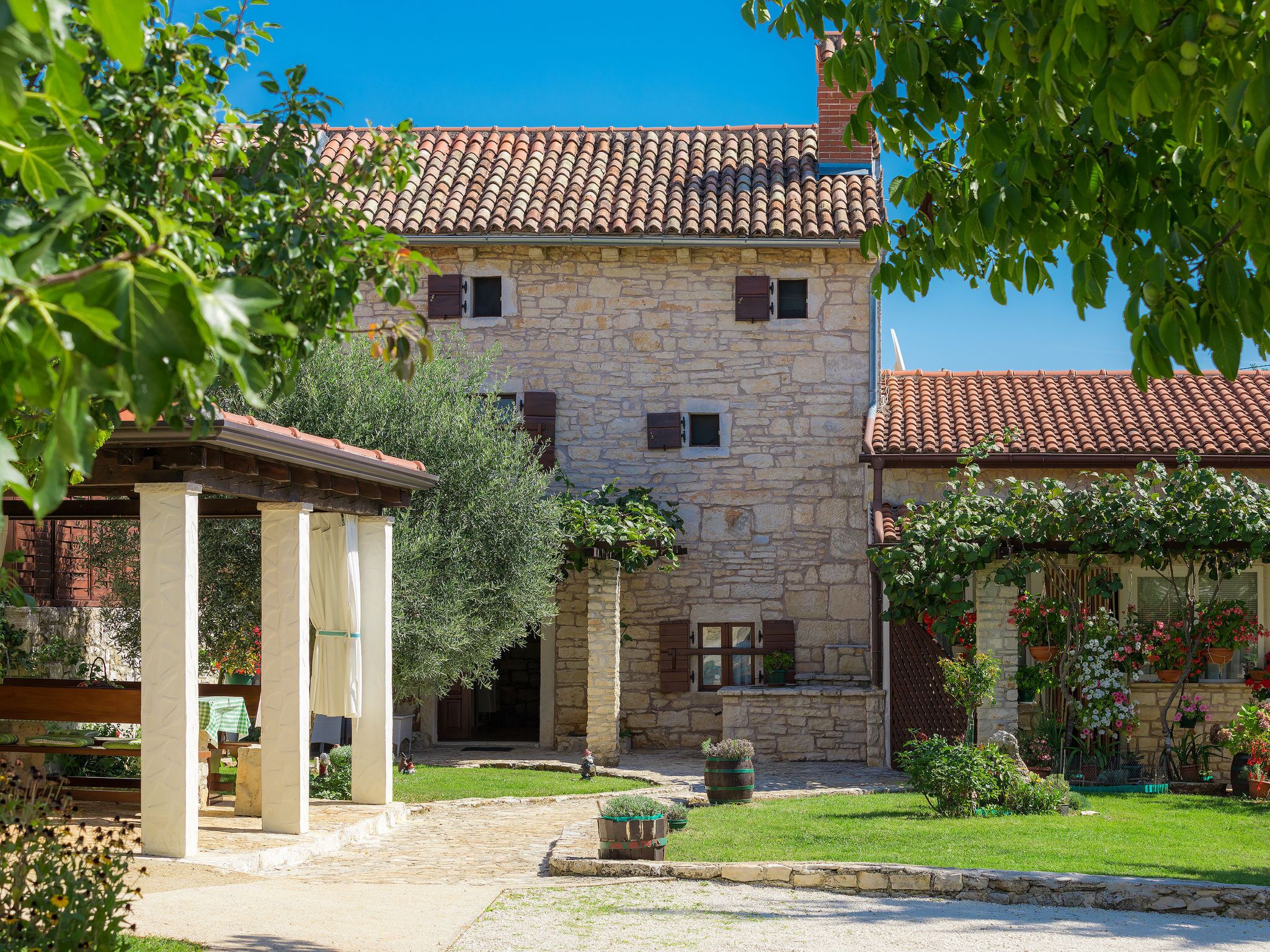 A stone building with a tiled roof, a covered outdoor seating area, and a well-maintained garden.