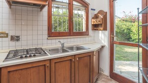 A kitchen with a gas stove, two sinks, wooden cabinets, a window with a view of greenery, and a door leading outside. - Gigli (REI226) by Interhome (Costa Rei)