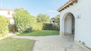 A stone-paved courtyard with a white building featuring an archway and a sign labeled "CANNAS". - Gigli (REI226) by Interhome (Costa Rei)