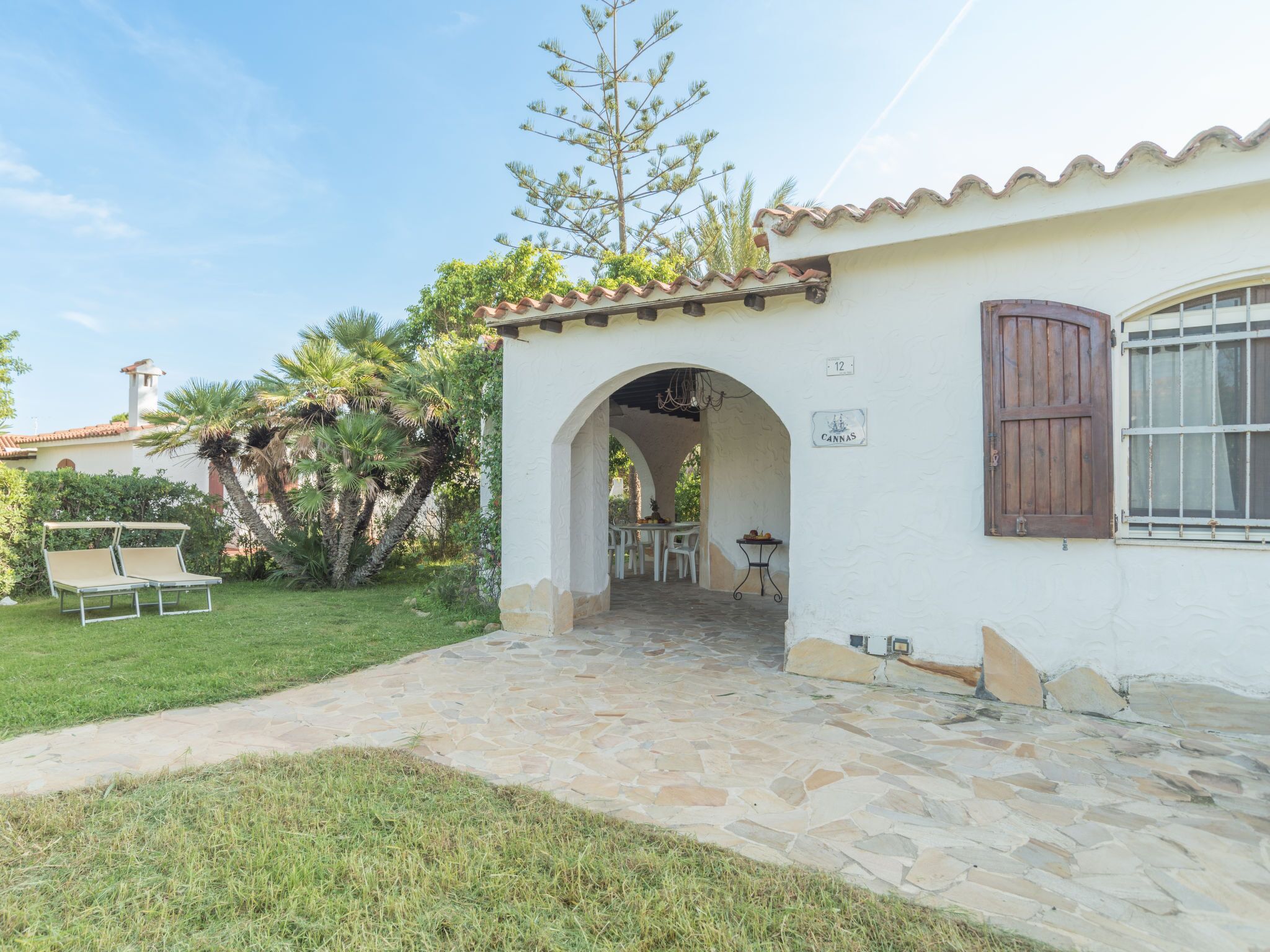 A white building with a stone pathway leading to an archway. There is a table and chairs outside the archway.