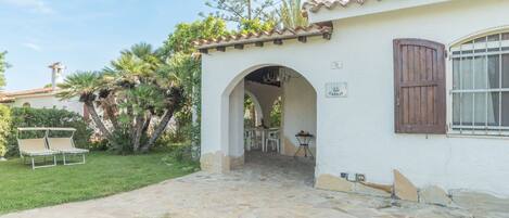 A white building with a stone pathway leading to an archway. There is a table and chairs outside the archway.