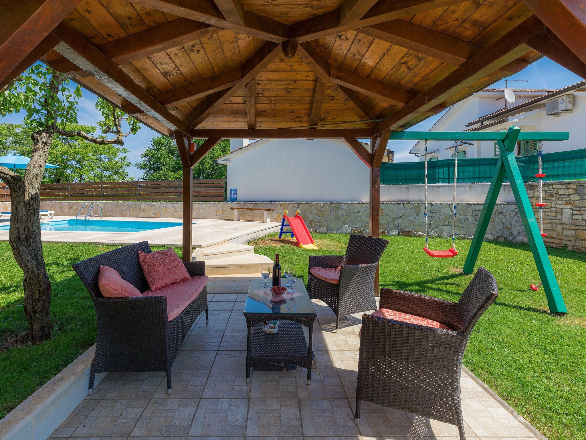 A covered patio area with wicker furniture, a pool, and a swing set.
