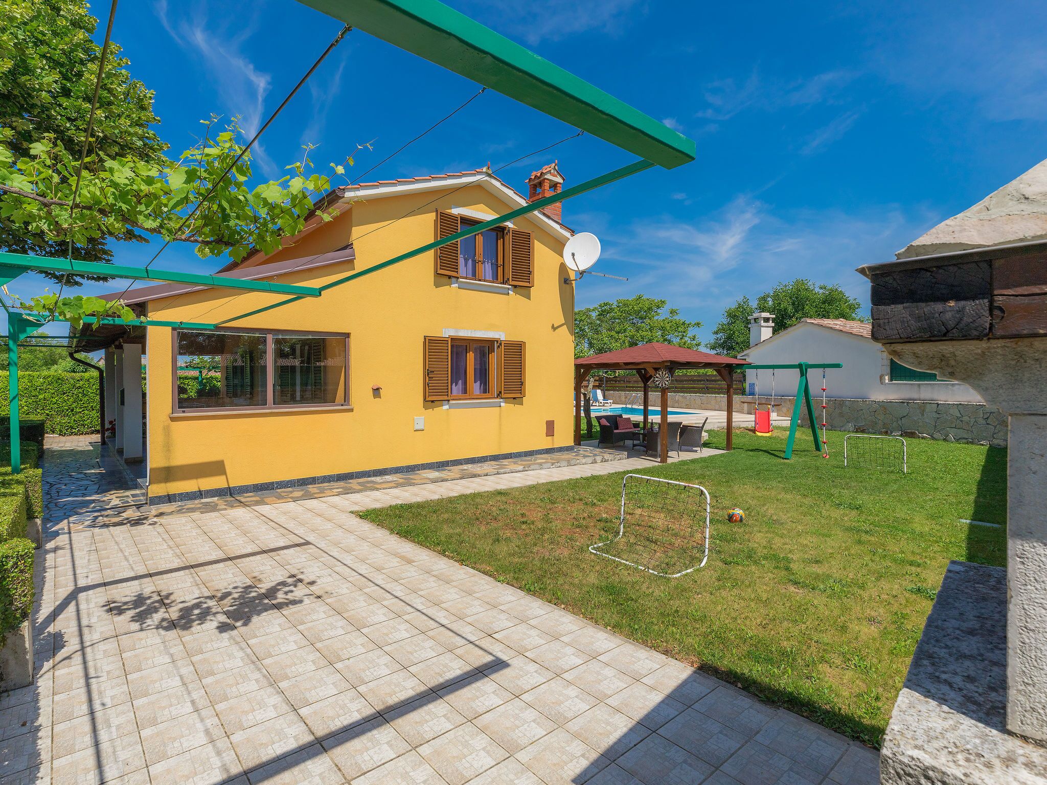 Una casa amarilla con un patio, piscina y un columpio.